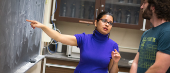 Woman teacher pointing at a black board while talking with student