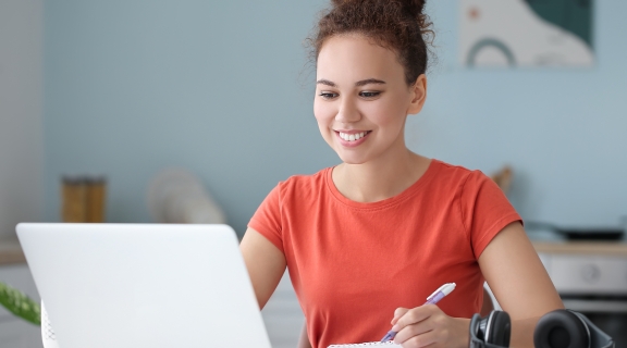 Woman writing while looking at a laptop